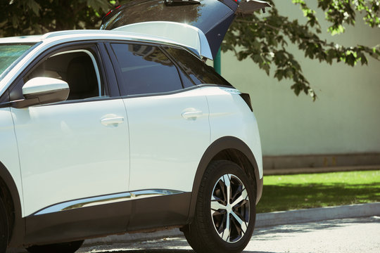 View of modern white car with the opened trunk on the city's street in sunny day. Weekend, preparation for holidays and vacation or business and working outdoors concept.