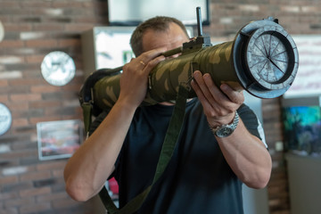 A man holds in his hands a rocket launcher assault grenade against a brown brick wall.
