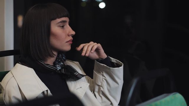Sad young woman looking out of a public transport window. Tired girl thinking of something sitting near the window. City lights background. Depressed concept.