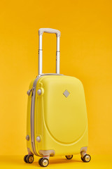 yellow travel bag with handle on wheels isolated on orange