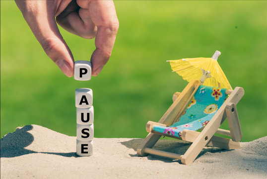 Am Sandstrand bilden W&uuml;rfeln das Wort "Pause" neben einer kleinen Sonnen-liege und einem Sonnenschirm.
