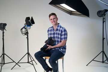 Portrait Of Male Photographer In Studio For Photo Shoot With Camera And Lighting Equipment