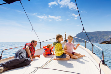Obraz premium Two little kid boys, father and toddler girl enjoying sailing boat trip. Family vacations on ocean or sea on sunny day. Children smiling. Brothers and sister, siblings and dad having fun on yacht.