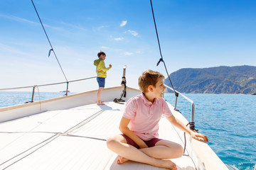 Two little kid boys, best friends enjoying sailing boat trip. Family vacations on ocean or sea on sunny day. Children smiling. Brothers, schoolchilden, siblings, best friends having fun on yacht.