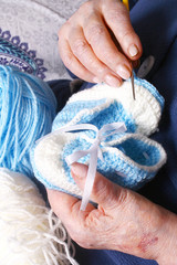 Grandma's hands are holding blue and white yarn and baby booties