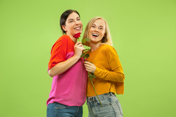 Portrait of pretty charming girls in casual outfits isolated on green studio background. Two female models as a girlfriends or lesbians. Concept of LGBT, equality, human emotions, love, relation.