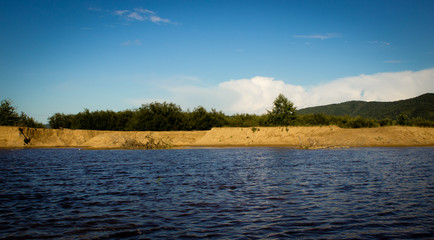 Summer landscape, forest and lake in green grass and sand, mountains and cloudy sky. summer in Russia.