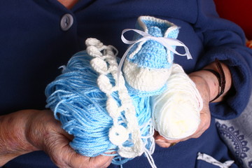 Grandma's hands are holding blue and white yarn and baby booties