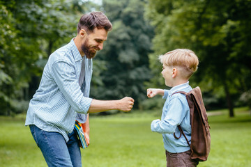 Image of a modern beard father giving a hi-five his little son in the park. Dad meets his son from...
