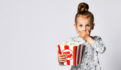 Portrait of a cheery pretty girl holding plastic cup and eating popcorn isolated over white...