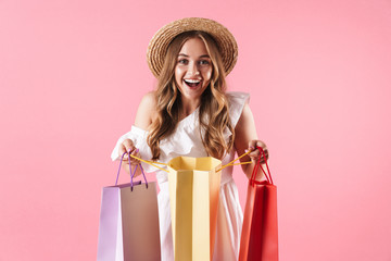 Image of caucasian amazed woman wearing straw hat wondering and holding shopping bags