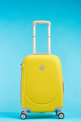 yellow colorful suitcase with handle on wheels on blue background