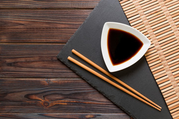 Chopsticks and soy sauce on black stone plate, wooden background with copy space