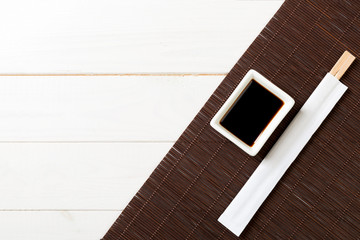 Bamboo mat and soy sauce with sushi chopsticks on white wooden table. Top view with copy space background for sushi. Flat lay