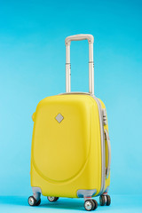 yellow colorful travel bag with handle on wheels on blue background