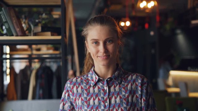 Portrait of cute young girl student wearing trendy shirt standing in cozy cafe smiling looking at camera alone. Happy millennials and cafeteria concept.