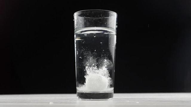 Effervescent aspirin tablet dropping to glass of water. Slow motion fizzy pill falls and dissolves with bubbles. Medicine, health care pharmacy chemistry concept