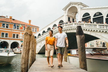 Fototapeta na wymiar Loving couple on vacation in Venice, Italy - Millennials visiting the famous Rialto Bridge while walking on the wooden pier