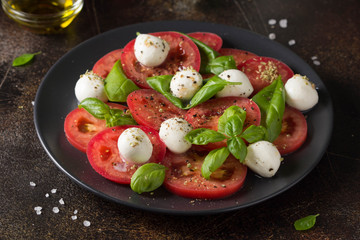 Caprese salad with mini mozzarella, juicy tomato and fresh Basil. Delicious Italian snack, traditional food. On dark background