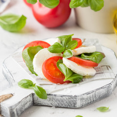 Caprese salad with mozzarella, juicy tomato and fresh Basil. Delicious Italian snack, traditional food. On light background
