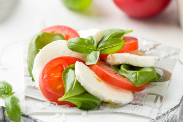 Caprese salad with mozzarella, juicy tomato and fresh Basil. Delicious Italian snack, traditional food. On light background