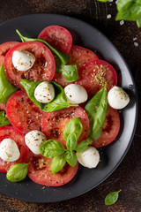 Caprese salad with mini mozzarella, juicy tomato and fresh Basil. Delicious Italian snack, traditional food. On dark background