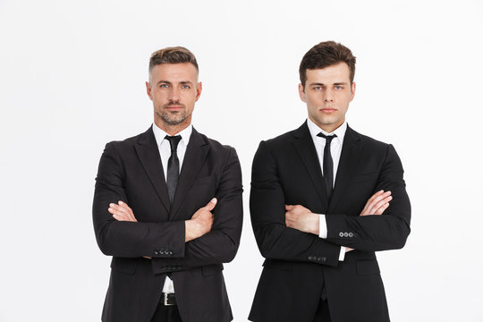 Image of masculine serious two businessmen in office suits looking at camera with arms crossed