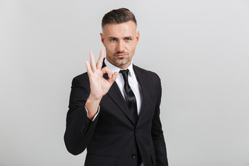 Image of confident adult businessman in formal suit gesturing ok sing