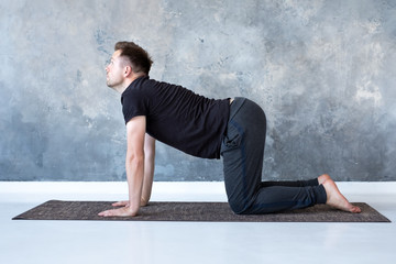 Young yogi men practices yoga asana bitilasana or cat cow pose