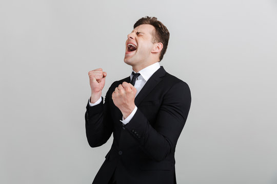 Image of joyful young businessman in formal suit screaming and clenching his fists