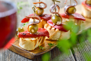 Spanische Pinchos mit Rotwein: Geröstetes Baguette mit eingelegter Paprika, gefüllten Oliven und Sardellenfilets - Spanish snack with red wine: Grilled bread with peppers, olives and anchovy fillets 