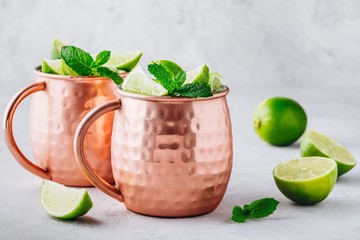 Moscow mule ice cold cocktail in copper cup with lime and and mint on gray stone background