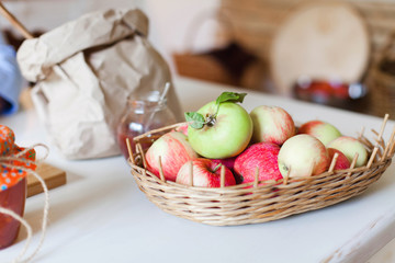 Apples in wicker basket, jam and flour are on wooden kitchen table. Autumn ingredients and fall harvest foods are prepared for cooking pie.