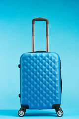 blue travel bag with handle on wheels on blue background