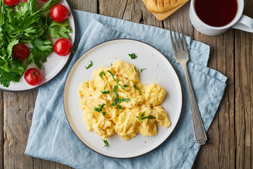 Scrambled eggs, omelette, top view. Breakfast with pan-fried eggs, cup of tea, tomatoes on old rustic wooden table