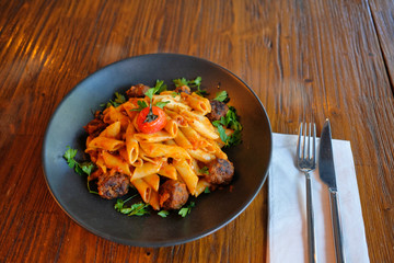 Penne pasta with meatballs in tomato sauce in a black bowl