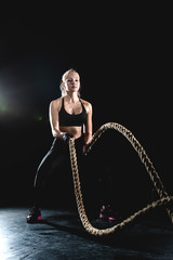 Beautiful athlete performs a rope exercise during a workout in the spotlight.