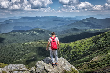 Obraz premium Traveler man with red backpack in mountains. Summer view forest, clouds