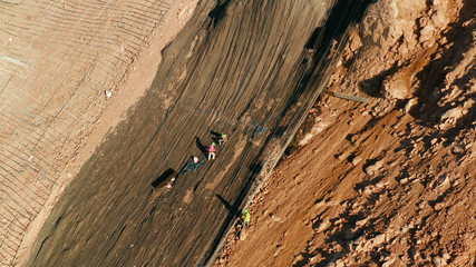 Fototapeta na wymiar Workers strengthen the slope of the mountain with metal mesh preventing rockfall and landslide on the road, above view. workers constructing anti-landslide concrete wall prevent protect against rock