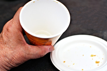 Seniors hand holding an empty coffee cup next to an empty paper plate