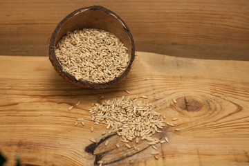 Raw oat grains in a coconut shell, low-calorie ingredient for delicious healthy breakfast on a wooden background, copy space. Nutritious whole grains, wholesome goodness and great tasting variety.