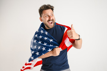 Celebrating an Independence day. Stars and Stripes. Young man with the flag of the United States of America isolated on white studio background. Looks crazy happy and proud as a patriot of his country