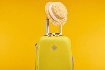 yellow colorful travel bag with sunglasses and straw hat on handle isolated on yellow