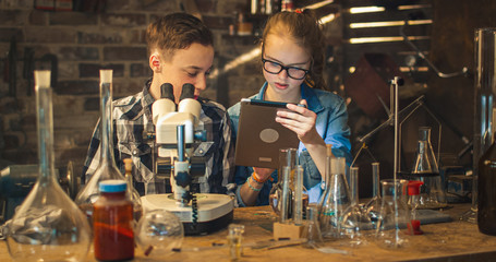 Young boy is making chemistry experiments while girl is looking at a tablet computer in a garage at home.
