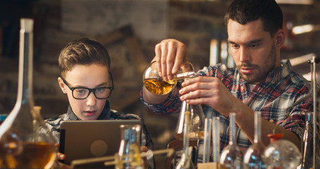 Father and son are making chemistry experiments while checking a tablet computer in a garage at home.