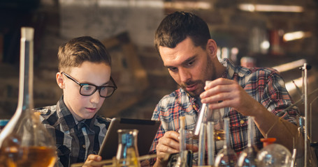 Father and son are making chemistry experiments while checking a tablet computer in a garage at home.