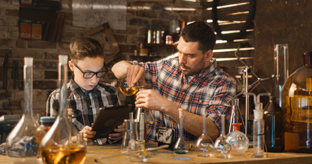 Father and son are making chemistry experiments while checking a tablet computer in a garage at home.
