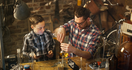Father and son are making chemistry experiments while checking a tablet computer in a garage at home.