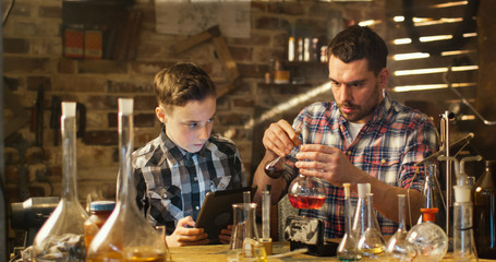 Father and son are making chemistry experiments while checking a tablet computer in a garage at home.