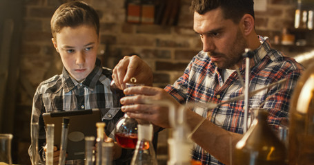 Father and son are making chemistry experiments while checking a tablet computer in a garage at home.